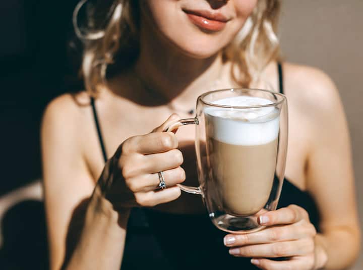 Kobieta trzymająca szklankę z latte z pianką - zdjęcie.